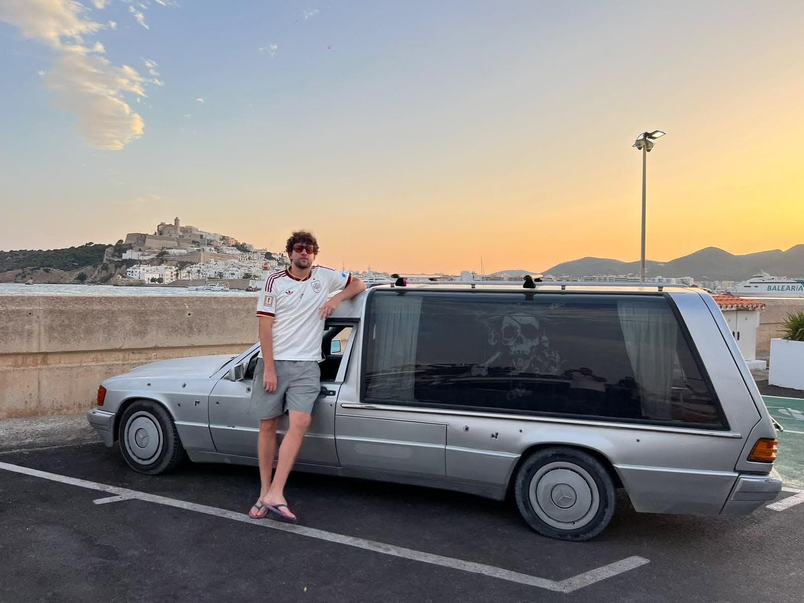 CaptainGee with the silver Mercedes hearse camper and pirate skull graphic at sunset